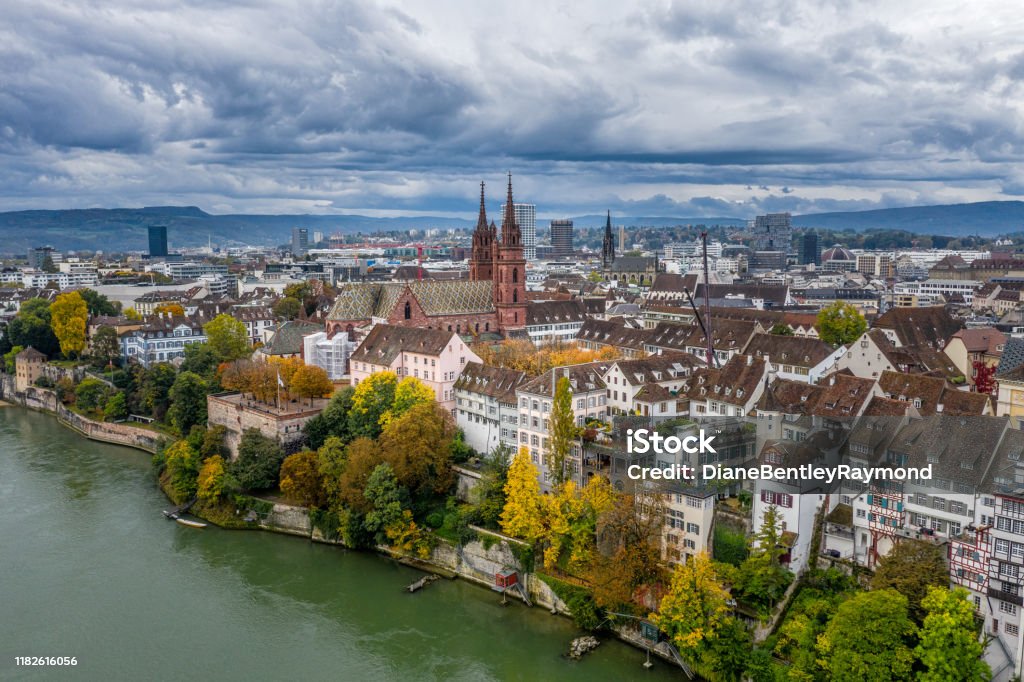 Aerial view of Basel Switzerland above the Rhine River An aerial view of the Basel Switzerland above the Rhine River. A view of Basler Munster Cathedral and it's tall spires in the morning light. A dramatic sky and bright Autumn colors along the shore. Basel - Switzerland Stock Photo