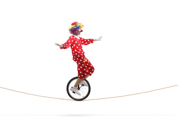 Full length profile shot of a scared clown riding a unicycle on a rope isolated on white background