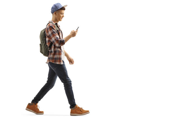 jonge kerel met een rugzak en pet wandelen en kijken naar zijn mobiele telefoon - alleen één tienerjongen stockfoto's en -beelden