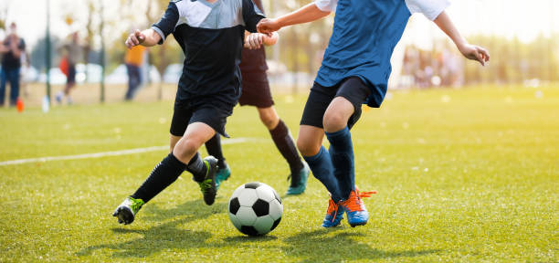 dois jogadores de futebol que funcionam e que retrocedem uma esfera de futebol. pés de dois jogadores de futebol novos em um fósforo. pernas européias do jogador da juventude do futebol na ação - competição desportiva juvenil - fotografias e filmes do acervo