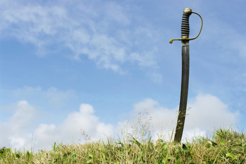 Antique Sabre Stuck In Grassy Ground Against Sky