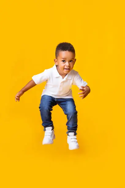 Photo of Adorable afro baby boy jumping over yellow studio background