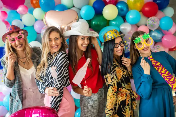 Female friends at Bachelorette party with photo booth props and balloons, smiling and having fun