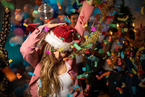 Dancing women with Santa hat celebrating New Yer with friends in night club, confetti all around