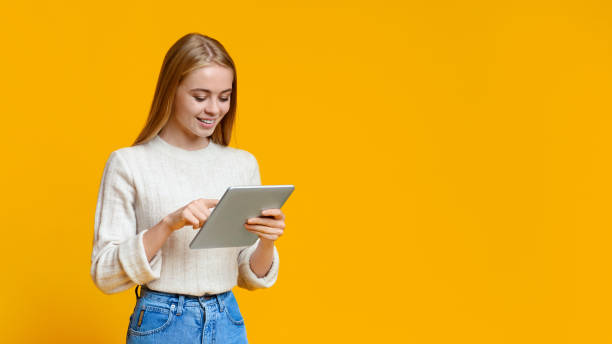 istock Beautiful teen girl using digital tablet over orange studio background 1182629310