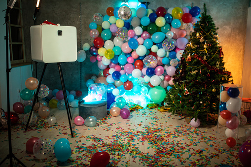 Room decorated for party, with photo booth , Christmas tree , wall with balloons, confetti on floor