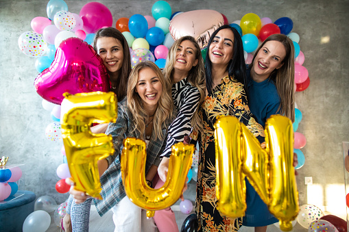 Joyful young women holding fun written with party balloons, smiling happily