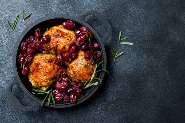 istock Roasted chicken legs with red grapes on pan over black slate stone background 1182630790