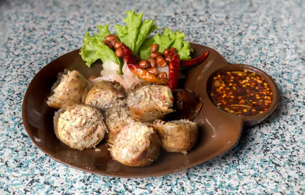 Photo of Sausage small circles on the grid-iron grill with smoke over charcoal. Thai sausage, fermented rice with pork sausage served with vegetables.