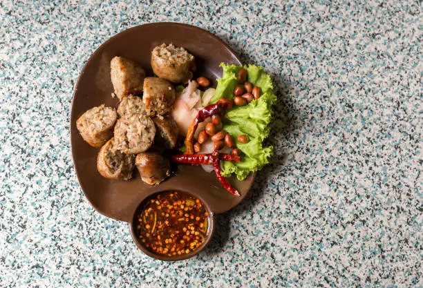 Photo of Sausage small circles on the grid-iron grill with smoke over charcoal. Thai sausage, fermented rice with pork sausage served with vegetables.