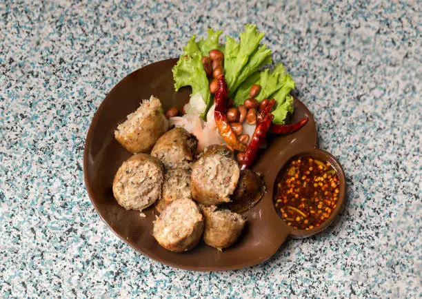 Photo of Sausage small circles on the grid-iron grill with smoke over charcoal. Thai sausage, fermented rice with pork sausage served with vegetables.