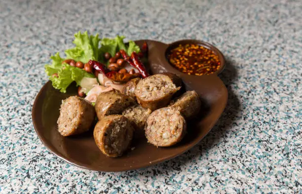 Photo of Sausage small circles on the grid-iron grill with smoke over charcoal. Thai sausage, fermented rice with pork sausage served with vegetables.