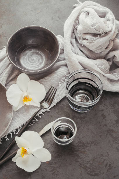 istock Elegance table setting with knitted grey napkin, cutlery, ceramic plates, glasses and white orchid flowers 1182636306