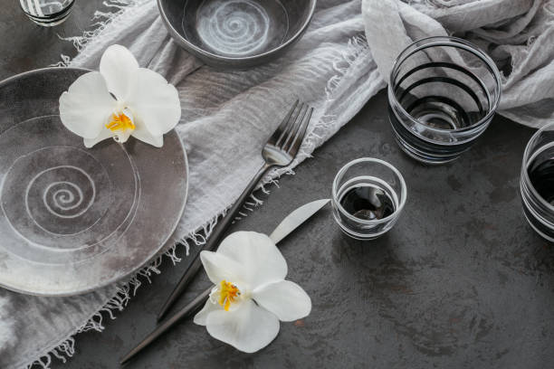 istock Elegance table setting with knitted grey napkin, cutlery, ceramic plates, glasses and white orchid flowers 1182636308