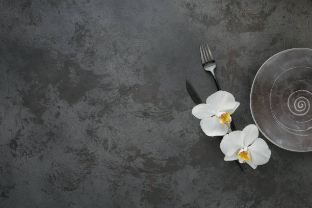 istock Elegance table setting with knitted grey napkin, cutlery, ceramic plates, glasses and white orchid flowers 1182636309