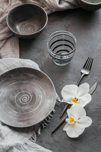 istock Elegance table setting with knitted grey napkin, cutlery, ceramic plates, glasses and white orchid flowers 1182636311