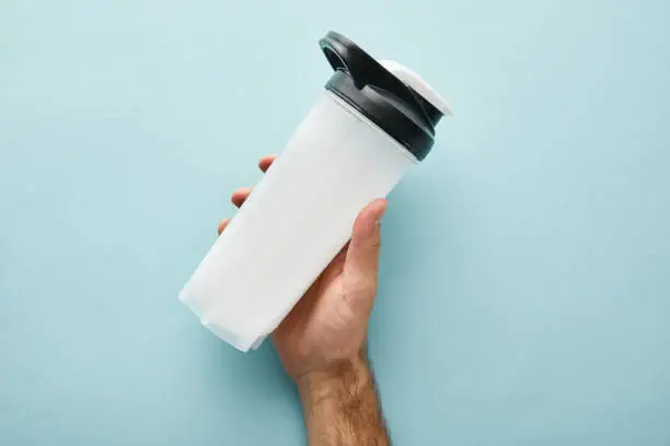 cropped view of man holding sports bottle with protein shake on blue