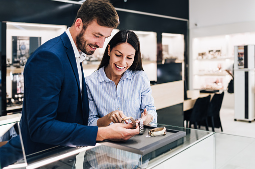 Beautiful couple enjoying in shopping at modern jewelry store while trying out and buying watches.