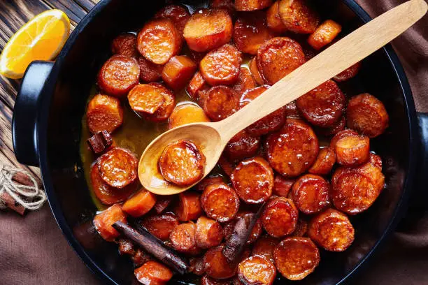 candied yams, sweet potatoes cooked with orange juice, cinnamon, brown sugar and butter in a black ceramic dish, top view, macro, flatlay