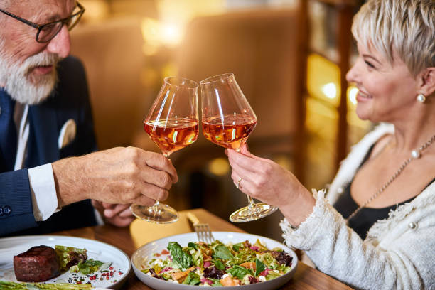 Modern couple have dinner and celebrate in restaurant Beautiful elderly couple have a meal in personable restaurant, in love. Grey-haired male and female drink and clink glasses with champagne. valentines day holiday stock pictures, royalty-free photos & images