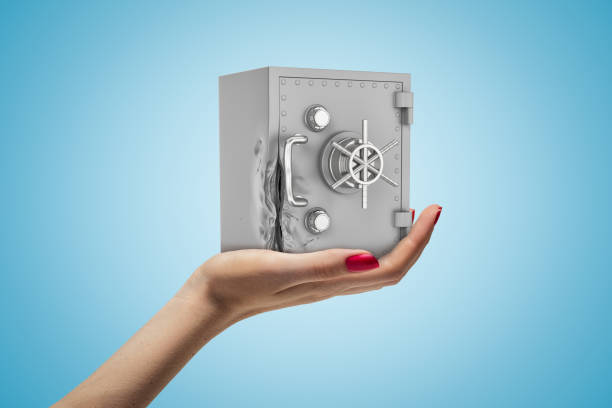 Side closeup of woman's hand facing up and holding light-grey safe on light-blue gradient background. Saving up. Banking business. Security systems.