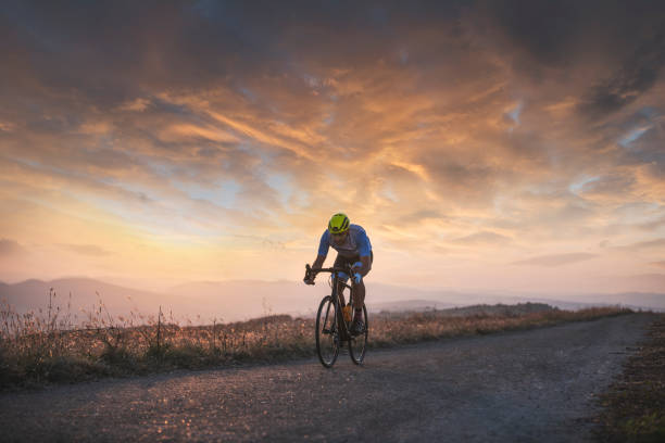 Athlete on racing bike outdoors at amazing sunset, he riding faster on the road.