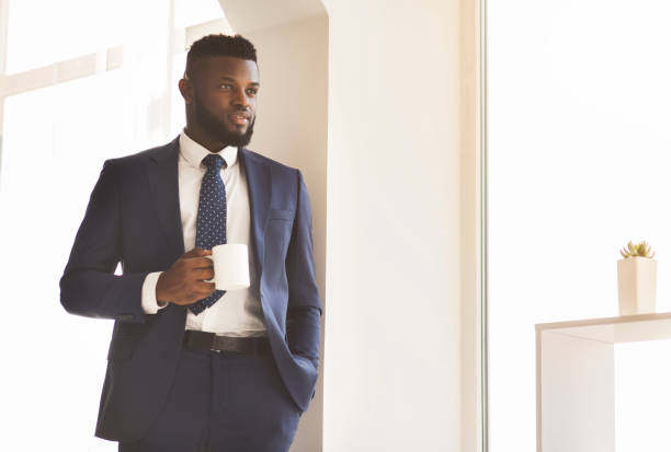 istock Handsome businessman drinking coffee next to window in office 1182642350
