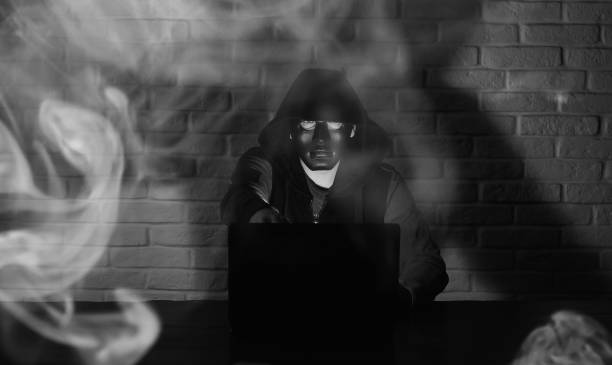 istock Hacker in black mask and hood at the table 1182642365