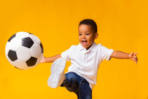 entzückende kleine junge fußballspielen, schlagen ball über gelben hintergrund - soccer child indoors little boys stock-fotos und bilder