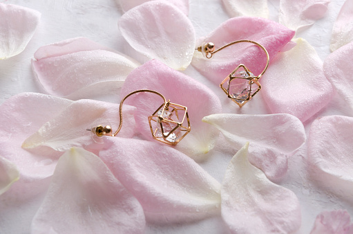 Top view of gorgeous pair of earrings with stones, pink roses petals on the white surface