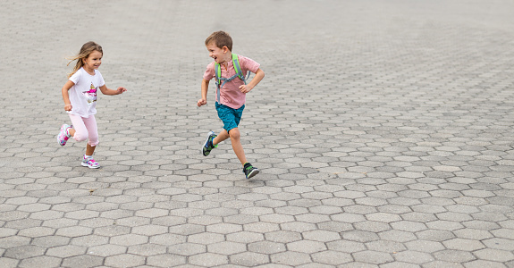 Children running in the city street. A boy and a girl have backpack.