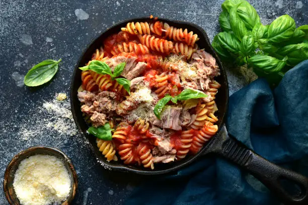 Fusilli pasta with tuna in tomato sauce in a skillet on a dark grey slate, stone or concrete background. Top view with copy space.