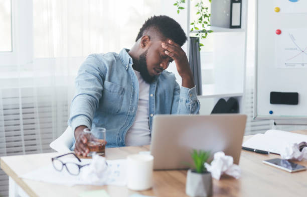istock Depressed black businessman drinking alcohol at workplace in office 1182647964