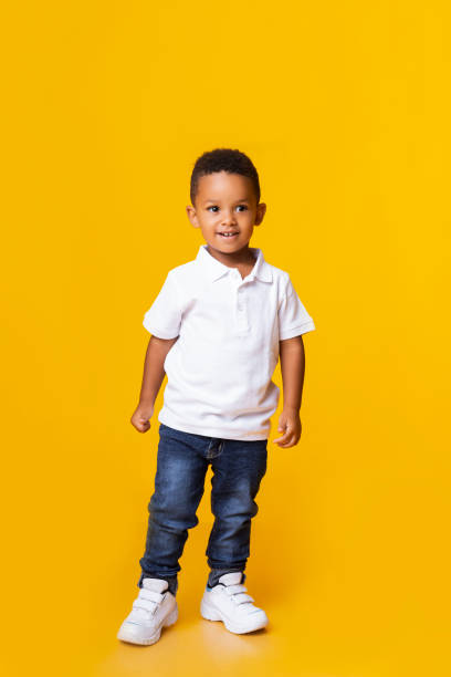 istock Cute little black boy standing in studio over yellow background 1182647978