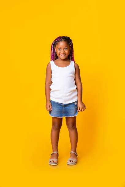 Portrait of cute little black girl with afro braids Portrait of cute little black girl with afro braids smiling and looking at camera while standing in studio over yellow background, copy space little black girl hairstyle stock pictures, royalty-free photos & images