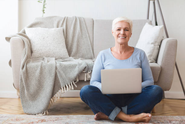 istock Active old woman sitting on floor and using laptop 1182648311
