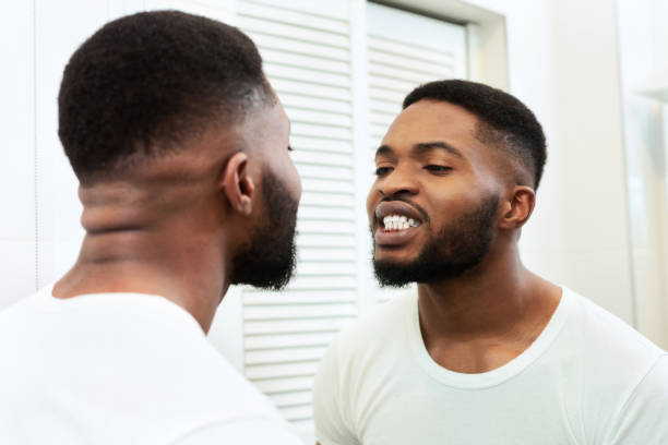 istock Young black man looking in mirror at his teeth in bathroom 1182649295
