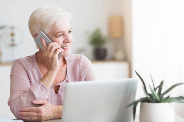 istock Positive old woman talking by phone with clients 1182649500