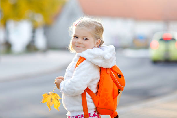 彼女の最初の日にかわいいかわいい幼児の女の子は、学校に行きます。保育園に歩いて健康な幸せな赤ちゃん。街の通りでデイケアに行くバックパックを持つ子供、屋外 - child little girls smiling autumn ストックフォトと画像