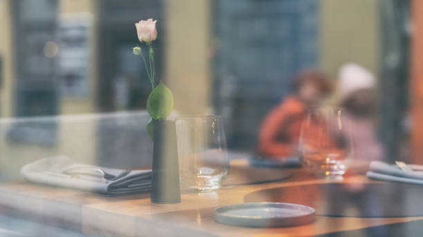 Reflection of passers-by on the street in a glass of a restaurant window-window with a table set and a flower in a vase in autumn.