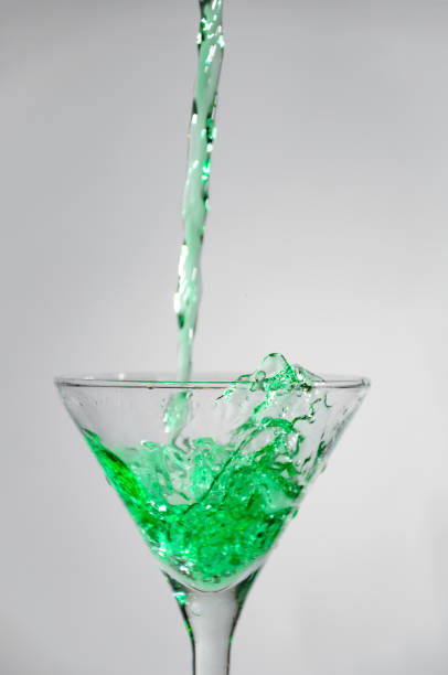 Splash of green liquid (cocktail, juice) pouring into the martini glass. Object on a white background.