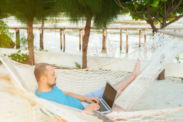 istock A man lying in a hammock overlooking the ocean. The guy with the beard working on laptop. 1182653432