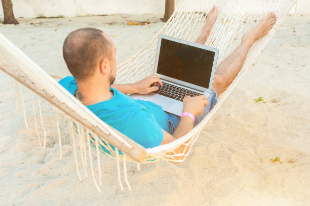 istock A man lying in a hammock overlooking the ocean. The guy with the beard working on laptop. 1182653509