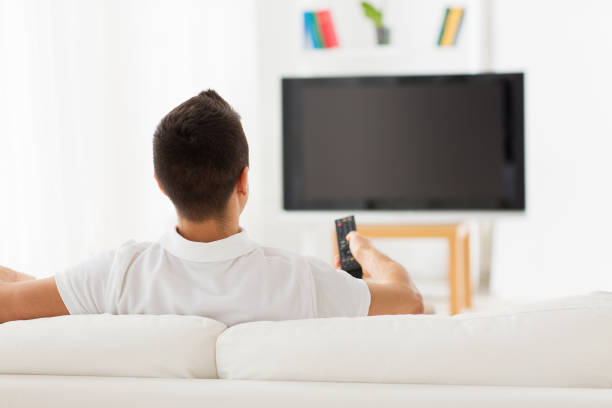 istock man watching tv and changing channels at home 1182654088
