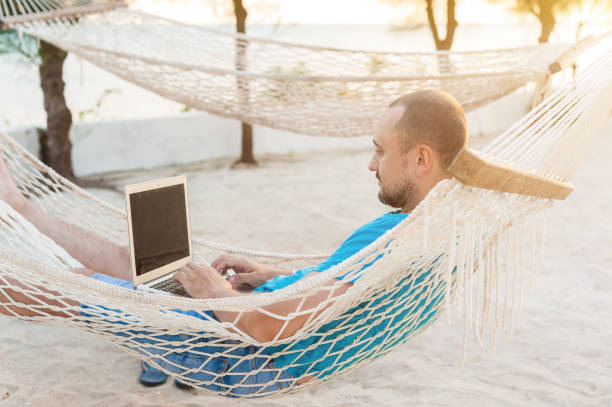 istock A man lying in a hammock overlooking the ocean. The guy with the beard working on laptop. 1182654179