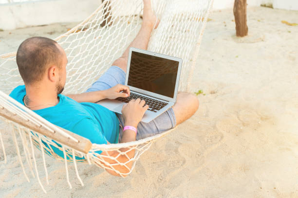 istock A man lying in a hammock overlooking the ocean. The guy with the beard working on laptop. 1182654195