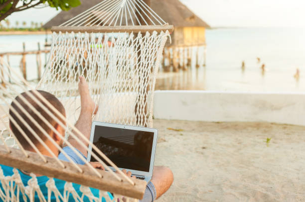 istock A man lying in a hammock overlooking the ocean. The guy with the beard working on laptop. 1182655043