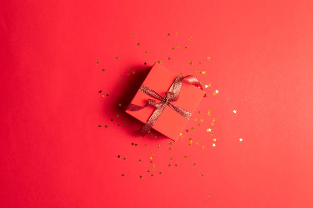 istock Minimal New Year concept. Creative composition of gift box with gold decoration bow on red background. Creative flat lay, top view design. 1182657604