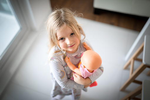 Portrait of an adorable little Indian girl obscuring her face while playing with a doll. Selective focus on face of the doll.