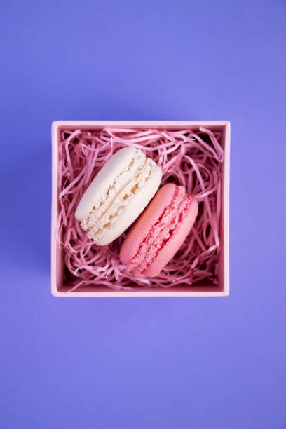 istock Two macaroons in pink box with decorative pink elements on a lilac color background. 1182667272